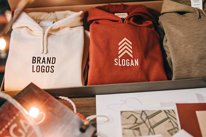 Boxed set of hoodies in white, red, and beige, featuring brand logos and slogans, alongside design materials.