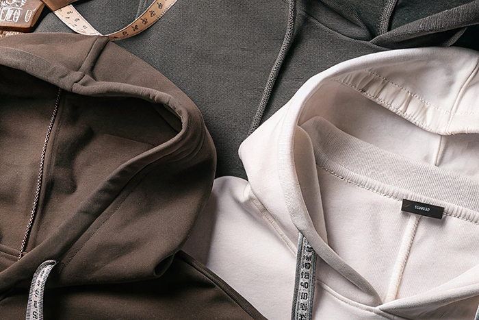 Close-up of neutral-toned hoodies with tailoring tools like scissors and measuring tape.