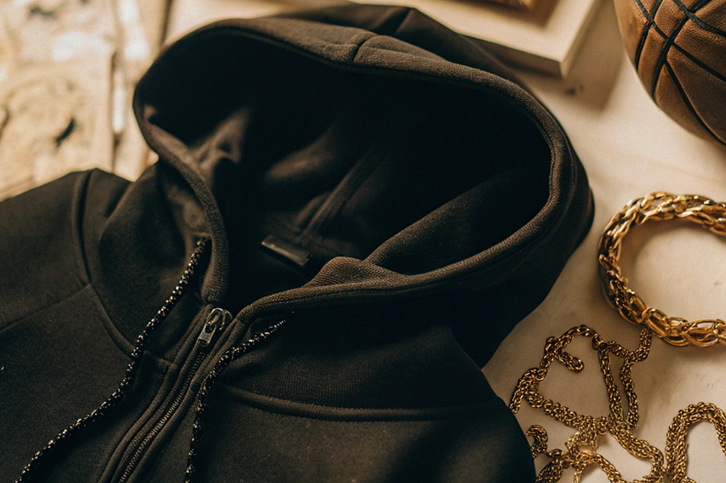 Black hoodie paired with sunglasses, a basketball, and gold chain accessories on a flat surface.