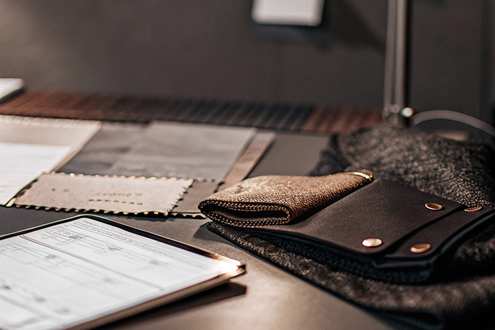 A designer's desk with fabric samples, a tablet, and leather accessories under focused lighting.