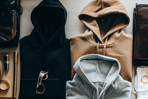 Flat lay of black, brown, and gray hoodies with matching accessories like shoes, glasses, and leather items.