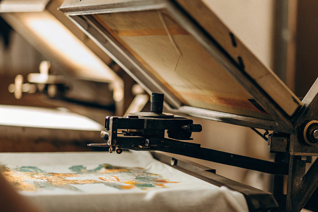 A screen printing press applying colorful designs on fabric in a workshop setting.