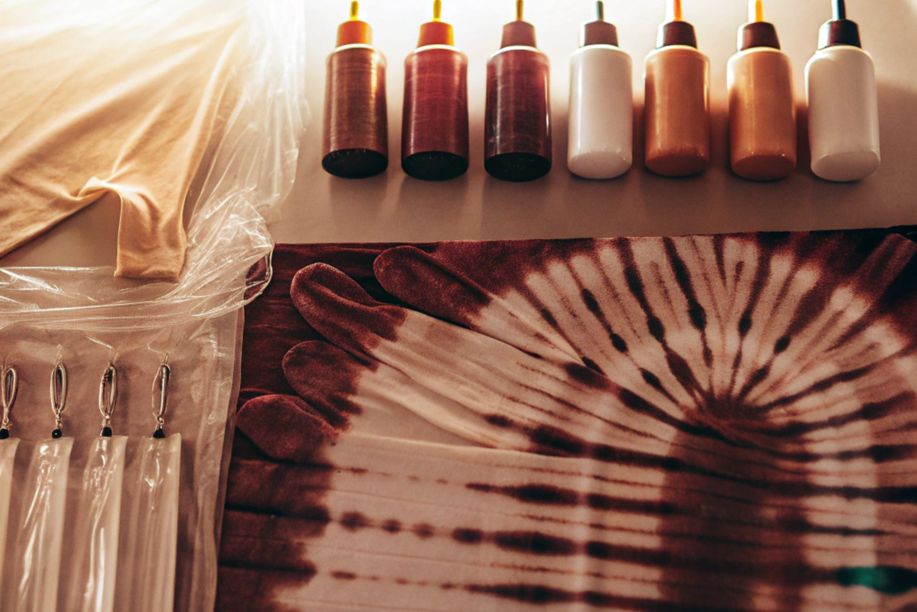 A flat lay of tie-dye materials including dye bottles, a t-shirt, plastic gloves, and a tie-dye pattern in progress.