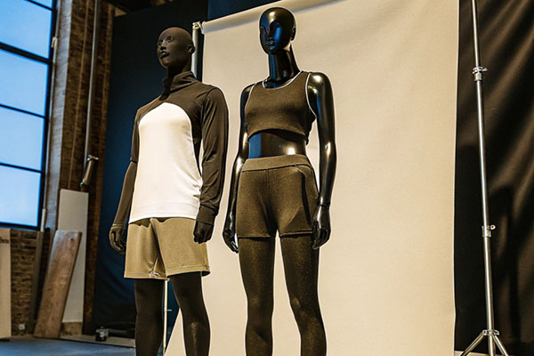 Two mannequins modeling athletic outfits: one in a long-sleeve top with shorts and another in a crop top with leggings, set against a studio backdrop.