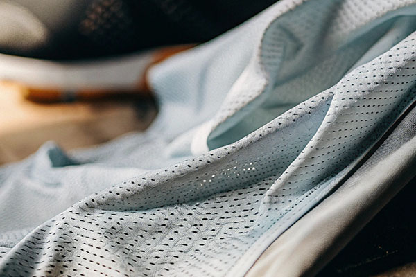 Close-up of light blue perforated fabric, designed for breathability, draped over a surface with sneakers in the background.