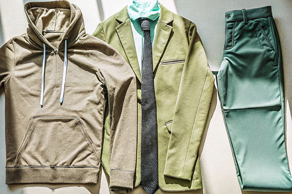 A beige hoodie, green suit jacket with tie, and green trousers laid out together, showcasing casual and formal clothing styles.