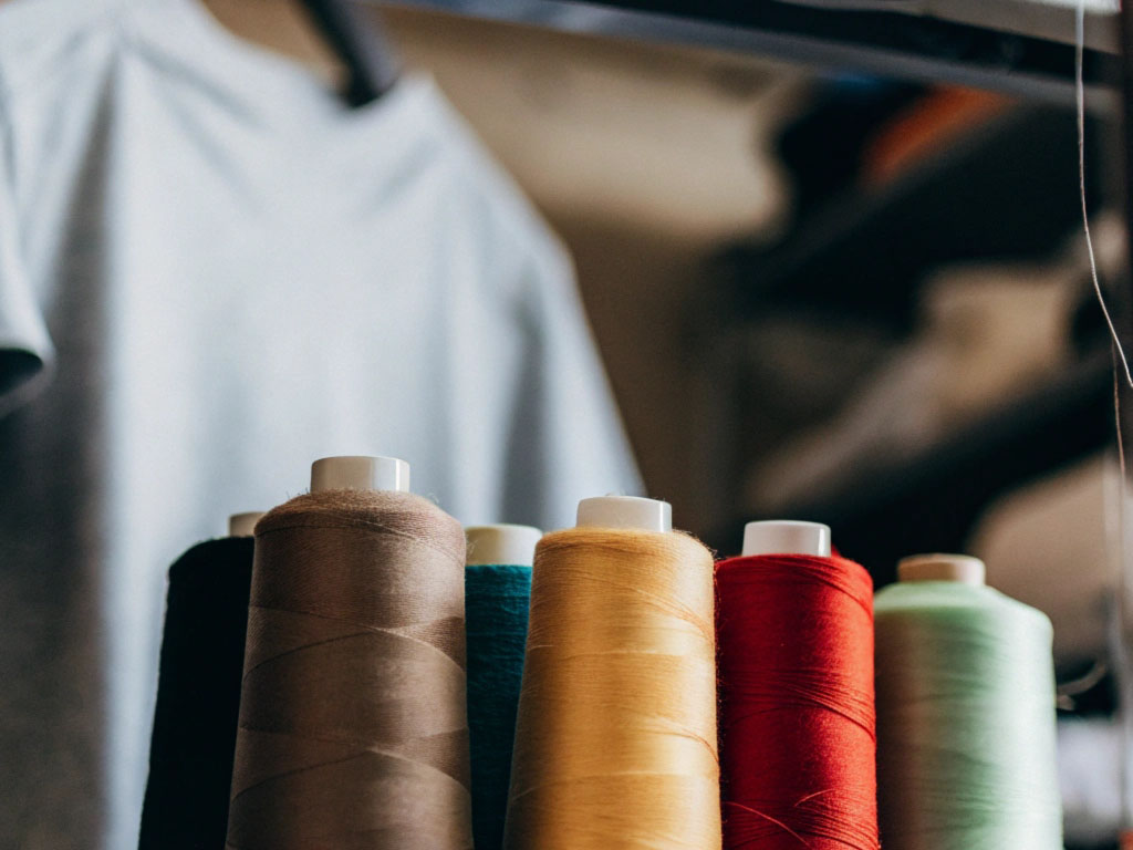 Spools of thread in brown, teal, yellow, red, and green arranged with a blurred sewing area and gray fabric in the background.