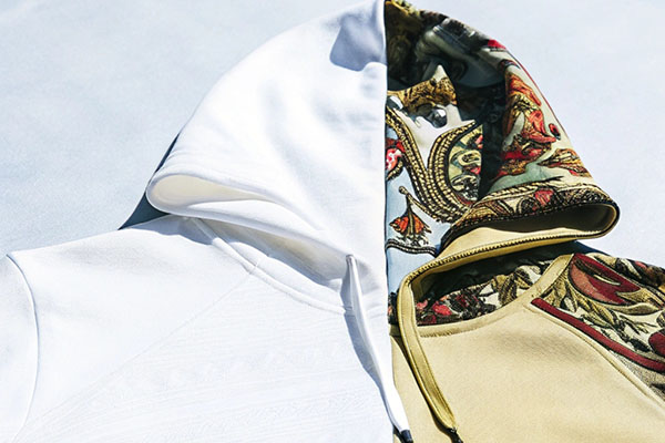 White hoodie contrasted with a beige hoodie featuring a colorful floral pattern on the interior hood, displayed on a light surface.