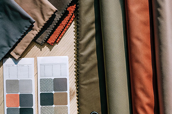 A selection of fabric rolls in earthy tones with corresponding color swatch cards on a wooden table.