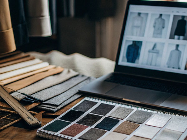 Fabric swatches and materials on a table with a laptop displaying clothing designs in a workshop setting.