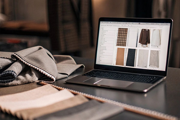 A laptop displaying fabric options alongside physical fabric swatches on a table in a modern workspace.