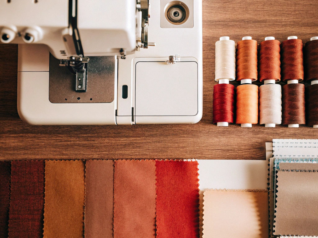 Sewing machine alongside fabric swatches in warm tones and spools of thread neatly arranged on a table.