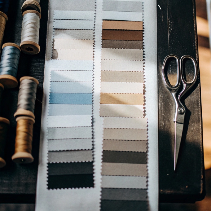 Neutral-toned fabric swatch samples with spools of thread and scissors on a dark table.