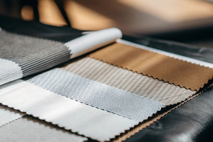 Close-up of assorted fabric swatches in white, beige, and gray tones displayed in soft light.