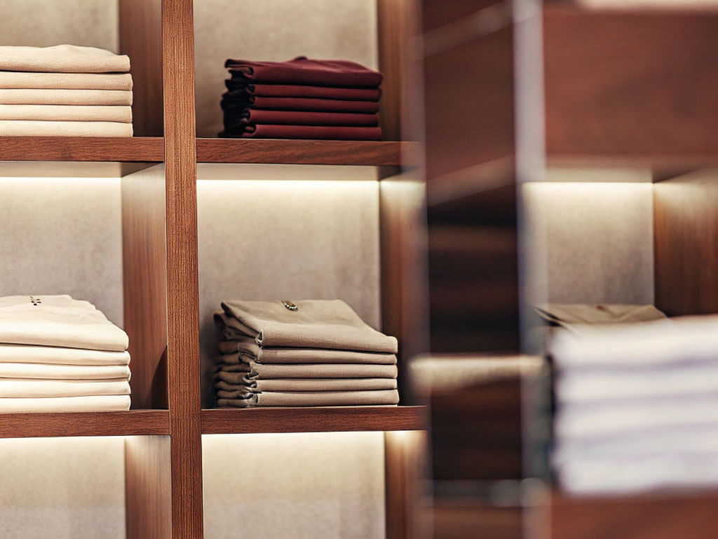 Neatly folded beige and maroon clothes stacked on wooden shelves with soft lighting in a retail display.