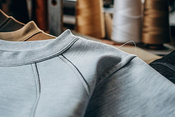 Close-up of a gray sweatshirt with detailed stitching, displayed near spools of thread in a workshop.