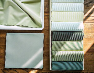 Selection of green fabric swatches, including plain and striped designs, displayed on a wooden table in natural light.