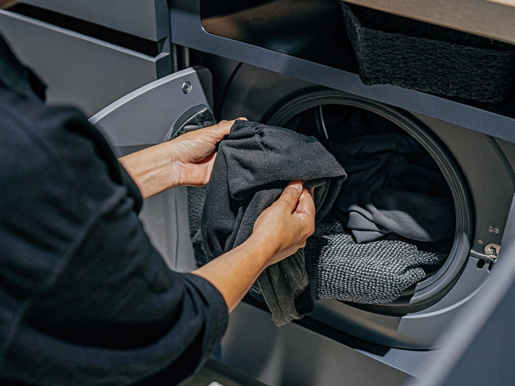 Person placing black and gray clothes into a front-loading washing machine, preparing for laundry.