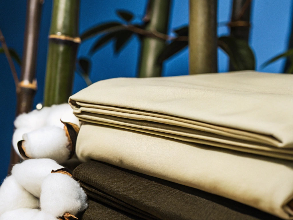 Neatly folded beige and olive fabrics with raw cotton branches against green bamboo and a blue backdrop.