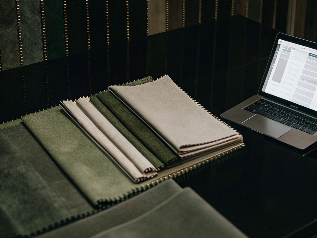 A collection of neutral and green fabric swatches on a black table next to an open laptop.