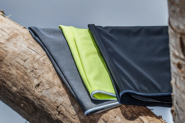 Folded fabric samples in black, gray, and neon green placed on a wooden log, showcasing texture and color contrast.