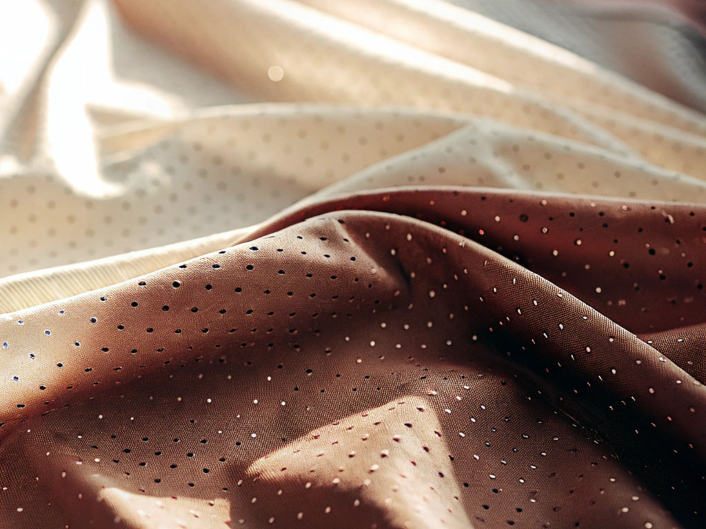 Soft beige and brown fabrics with subtle polka-dot patterns, illuminated by natural light.