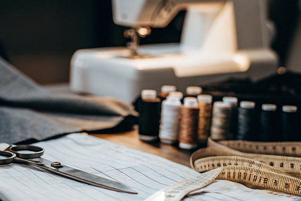Sewing workspace with a sewing machine, spools of thread, fabric, measuring tape, and scissors on a table.