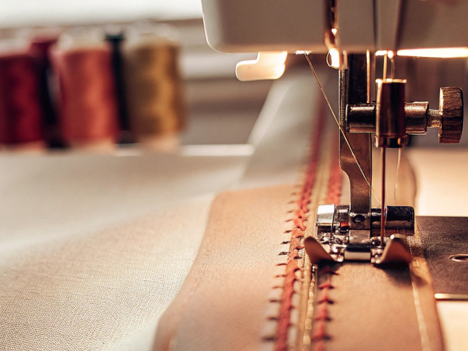 Close-up of a sewing machine stitching fabric with colorful thread spools in the background.