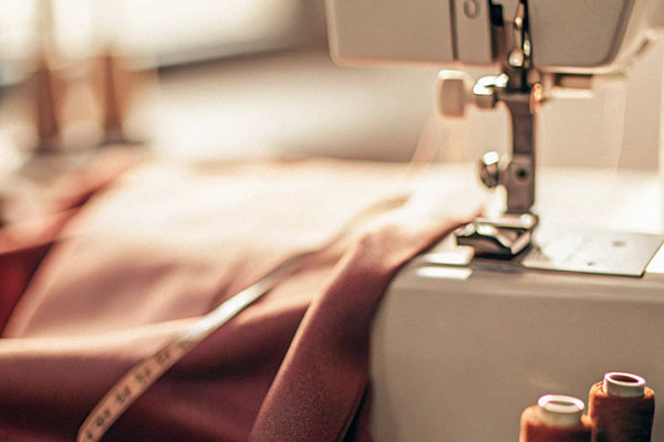 Sewing machine with fabric, a measuring tape, and spools of thread on a wooden table in warm light.