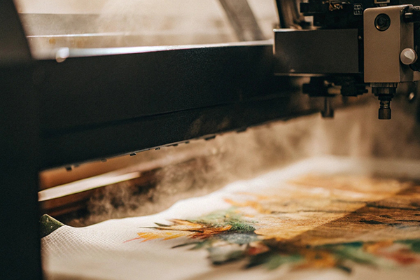 A close-up of a fabric printer creating a vibrant floral design on cloth with visible steam.