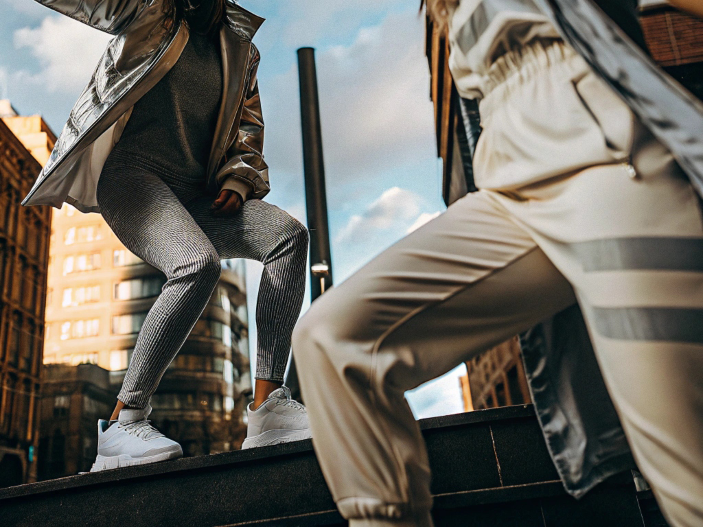 Two women wearing stylish activewear and metallic jackets posing outdoors in a modern cityscape.