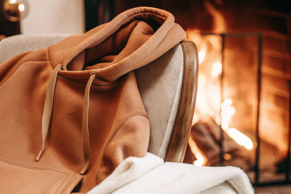 A brown hoodie draped over a chair near a cozy fireplace, creating a warm and relaxing atmosphere.
