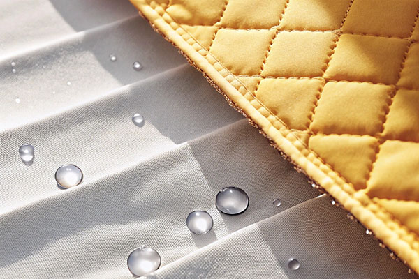Close-up of quilted yellow fabric paired with white water-repellent material, showing water droplets beading on the surface.