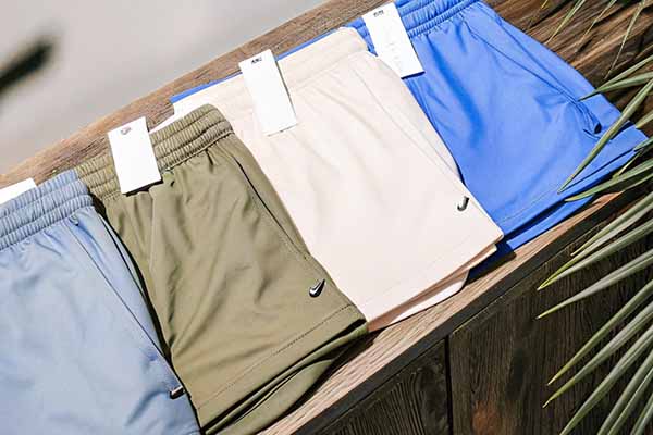 Row of athletic shorts in blue, green, beige, and bright blue, neatly displayed on a wooden surface under sunlight.