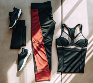 Flat lay of black and red activewear, including leggings, a fitted sports top, and black sneakers, arranged on a sunlit surface.