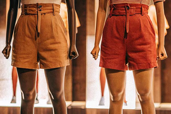 Mannequins wearing khaki and black casual shorts paired with neutral tops, displayed under bright lighting against a blue backdrop.