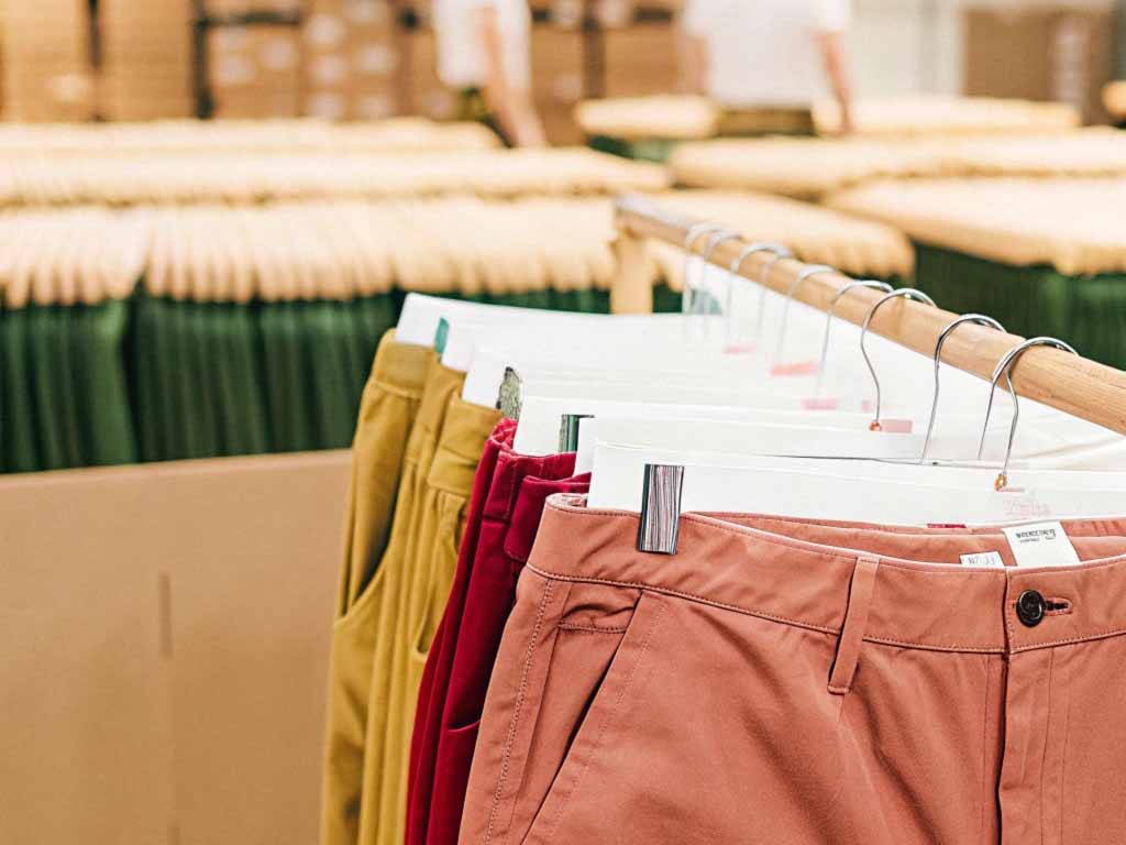 Rack of colorful pants, including red, mustard, and terracotta shades, displayed in a well-lit clothing store.