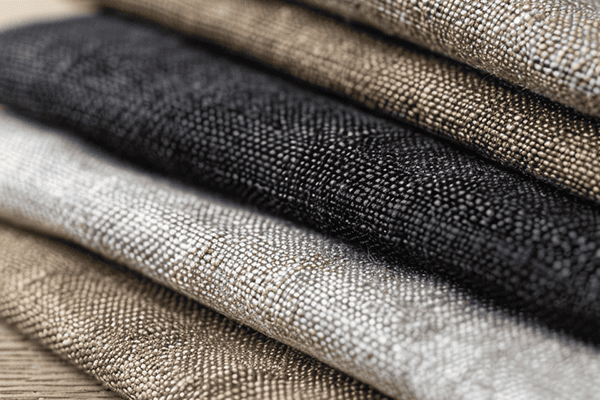 Close-up of stacked woven fabric swatches in shades of beige, black, and gray, showcasing textured patterns and natural tones.