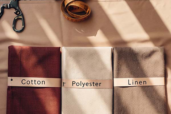 Cotton, polyester, and linen fabric samples neatly folded, labeled, and displayed with a tape measure and scissors nearby.