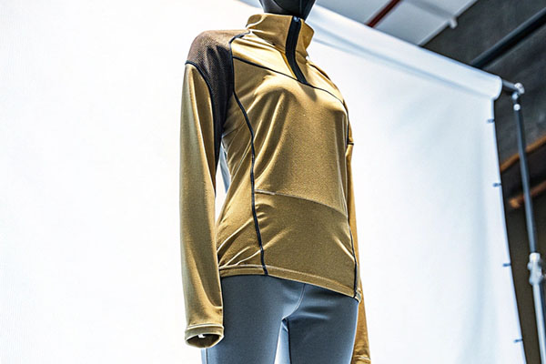 Mannequin dressed in a gold long-sleeve athletic top with black accents and gray leggings, set against a studio backdrop.
