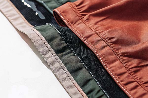 Close-up of stacked athletic shorts in beige, green, and orange with detailed stitching.
