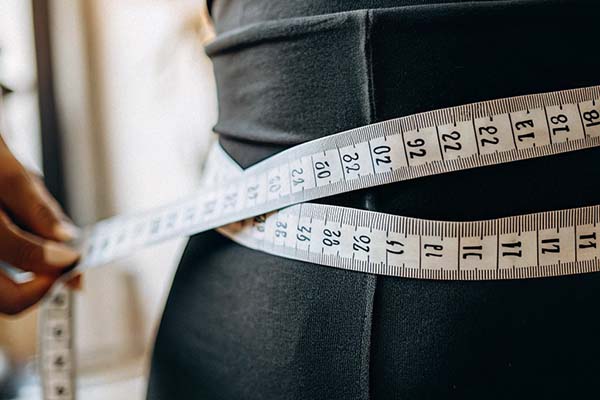 Close-up of a measuring tape wrapped around a person’s waist wearing black fabric.