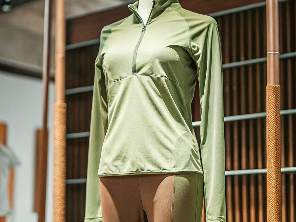 Mannequin showcasing a fitted olive green long-sleeve athletic top paired with beige leggings in a retail environment.