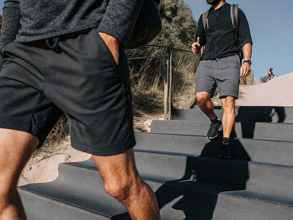 Two men in black and gray athletic shorts walking down outdoor steps in a sunny natural setting.