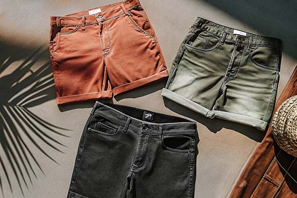 Three pairs of rolled-up shorts in earthy tones—red, green, and black—styled on a flat surface with natural light and shadows.