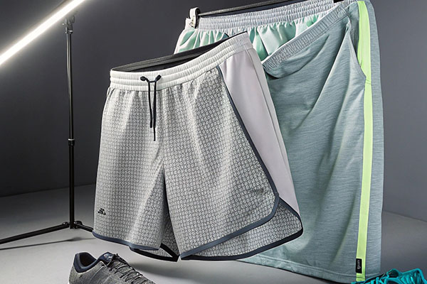 Two pairs of gray and green athletic shorts displayed with matching shoes and lighting.