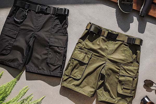 Black and olive-green tactical cargo shorts with belts and multiple utility pockets, styled outdoors.