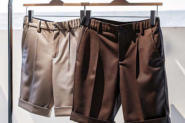 Beige and brown tailored shorts with cuffed hems hanging on a rack in bright natural light.
