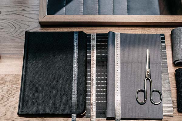 Fabric swatches, scissors, and measuring tape arranged neatly on a wooden table for tailoring.