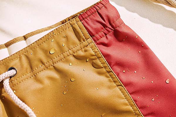 Close-up of yellow and red swim shorts with water droplets, highlighting their quick-dry and water-repellent fabric.